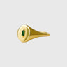 Gold Montego ring with a green gemstone on a beige background