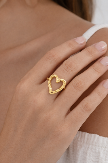 Gold heart-shaped ring on a person's finger with a neutral background