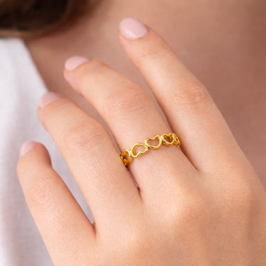 Gold ring with a unique design on a person's finger against a neutral background