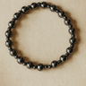 Offset Bracelet — polished gunmetal hematite beaded bracelet with mirror finish on beige surface, minimal and reflective by Matte.