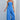 Model wearing the Oriana Jumpsuit in bright blue strapless wide-leg design against a light gray background.