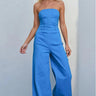 Model wearing the Oriana Jumpsuit in bright blue strapless wide-leg design against a light gray background.