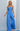 Model wearing the Oriana Jumpsuit in bright blue strapless wide-leg design against a light gray background.