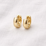 Orix Huggie Earrings – chunky gold huggie earrings with a smooth polished gold finish, photographed on a soft neutral background.