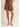 Ragit Short chocolate brown tailored pleated shorts front view, featuring high-rise waist, structured pleats, soft draped fabric, and relaxed A-line leg opening styled with flat sandals.
