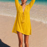 Ray Cover Up lightweight yellow beach cover-up with relaxed flowy silhouette, long sleeves, and deep V neckline, worn over swimwear on the beach.