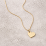 Rebecca Necklace featuring a softly hammered gold heart pendant on a fine chain laid on a neutral background.