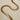 A gold-plated necklace with a herringbone chain design laid out on a plain surface.