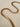 A gold-plated necklace with a herringbone chain design laid out on a plain surface.