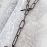A black enamel necklace with a chain link design, displayed on a textured surface.