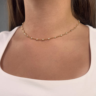 Woman wearing Rhodes Necklace, delicate gold chain with bezel-set pearls, styled with white top