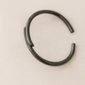 Gunmetal open cuff bracelet with sculptural design on beige linen background.
