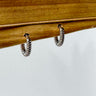 A pair of Sabina gold-plated huggie earrings displayed on a wooden surface.