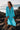 Schiro Cover Up turquoise flowy beach cover-up with relaxed silhouette, long sleeves, and deep V neckline worn on rocky beach.