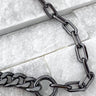 A close-up of a black enamel necklace with a Cuban chain link design placed on a textured surface.