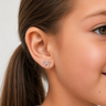 Young girl wearing Silver Bow Stud Earrings in polished silver with delicate open-loop bow design and mirror finish, styled in a clean close-up portrait with soft neutral lighting.