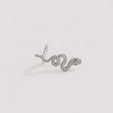 Snake Ear Cuff in polished silver featuring a crystal pavé serpent silhouette with green stone eyes, designed as a bold statement ear cuff on a soft neutral background.