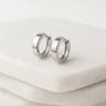 Silver minimalist huggie hoop earrings on white marble background – Stella Huggie Earrings by Matte