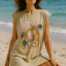 Woman on a beach wearing a beige sleeveless shirt with a tiger graphic and text.