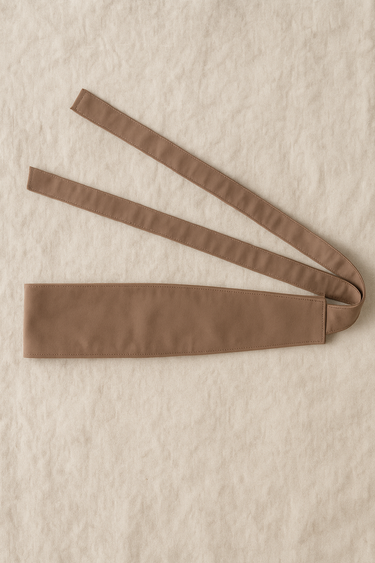 Taupe wrap belt displayed flat on beige linen background.