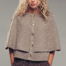 Model wearing neutral knit cape cardigan with oversized buttons and textured fabric, front view.
