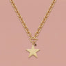 Close-up of model wearing Twinkle Necklace, a chunky gold chain necklace with oversized star pendant and small celestial charm, styled with a neutral knit top