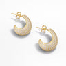 Vela Pavé Hoop Earrings gold pavé hoop earrings front angled view showing curved sculptural shape and full crystal detailing on light gray background.