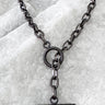 A black enamel necklace with a chain link design displayed against a textured grey background.