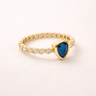 Voluspa Ring gold band with blue pear-shaped gemstone on neutral background