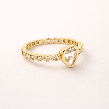 Voluspa Ring gold band with clear pear-shaped gemstone on neutral background