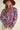 Woman walking outdoors wearing sky blue floral knit sweater with pink floral design, paired with hat and corduroy pants.