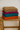 Stack of colorful Eto Pashminas on a wooden stool against a white wall.
