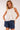 Model wearing Yui Sleeveless Ruffle Detail Top in white cotton with front ruffle detail, styled with denim shorts.