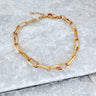 A gold-colored bracelet with a chain link design, displayed on a grey surface.