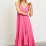 A woman standing in a studio setting, wearing a pink midi dress with spaghetti straps and a ruffled hem.