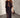 A woman wearing a black maxi dress with sheer details and a beaded design, standing in a room with a minimalist decor.