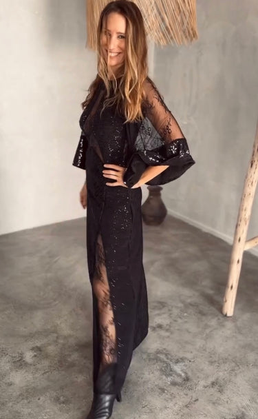Woman wearing sheer black Ammica Maxi Dress with beaded details indoors under soft light.