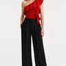 Woman wearing the Anisa red one-shoulder ruffle top with black wide-leg trousers, front view.