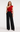 Woman wearing the Anisa red one-shoulder ruffle top with black wide-leg trousers, front view.