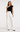 Woman wearing the Anisa black one-shoulder ruffle top styled with ivory wide-leg trousers.