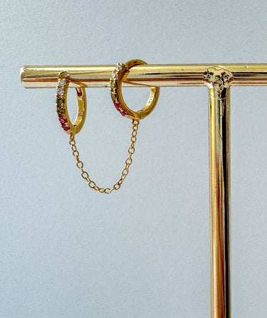 Annelis Huggie Chain Earrings in gold displayed on a gold stand against neutral background.