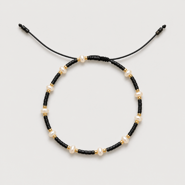 Arinet Bracelet in black featuring faceted dark gray beads, freshwater pearls, polished gold spacer beads, and an adjustable black cord closure.