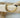 A gold-colored bracelet with a mix of solid and patterned beads displayed on a wooden surface by Matte