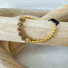 A gold-colored bracelet with a mix of solid and patterned beads displayed on a wooden surface by Matte