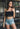 A woman wearing a black lace bralette and denim shorts.