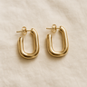 Gold sculptural oval huggie earrings on white linen backdrop, Bloro Huggie Earrings.