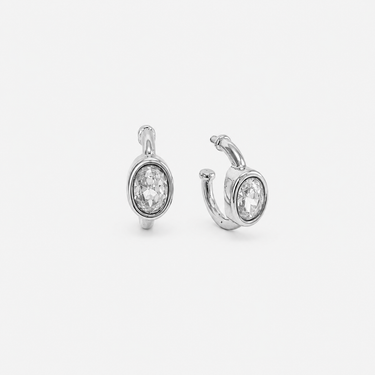 Braine Hoop Earrings featuring polished silver-plated hoop earrings with a bezel-set oval clear crystal charm, smooth rounded hoop silhouette, high-shine finish, secure hinged closure, lightweight design, and an elegant everyday style.