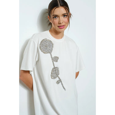Woman wearing a white oversize  t-shirt with a silver floral design on a plain background
