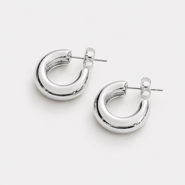Carda Hoop Earrings featuring polished silver-plated chunky hoop earrings with a smooth rounded silhouette, mirror finish, bold tubular design, secure hinged closure, lightweight feel, and timeless everyday style, displayed on a soft white background.