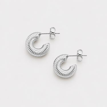 Caroline Hoop Earrings featuring polished silver chunky hoop earrings with a textured ribbed finish, rounded silhouette, mirror shine, secure post-back closure, lightweight design, and bold everyday style, displayed on a soft white background.